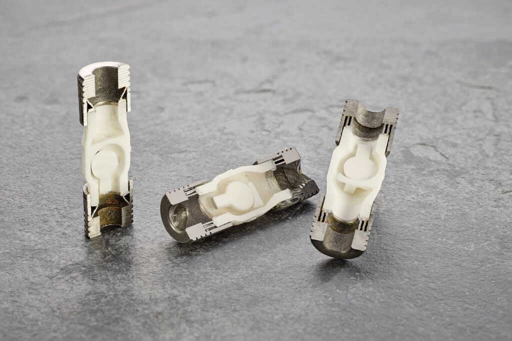 Three hybrid check valves made from 3D-printed alumina ceramics and stainless steel, shown in different positions on a gray surface