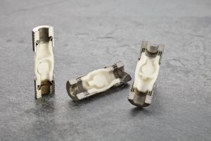 Three hybrid check valves made from 3D-printed alumina ceramics and stainless steel, shown in different positions on a gray surface